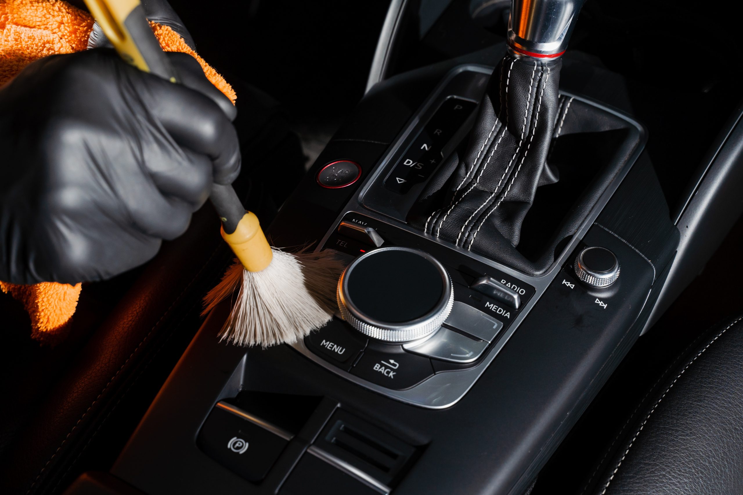 Dry cleaning with brush of gearbox and dashboard in car. Auto detailing service. Cleaning individual elements of black leather interior in auto.